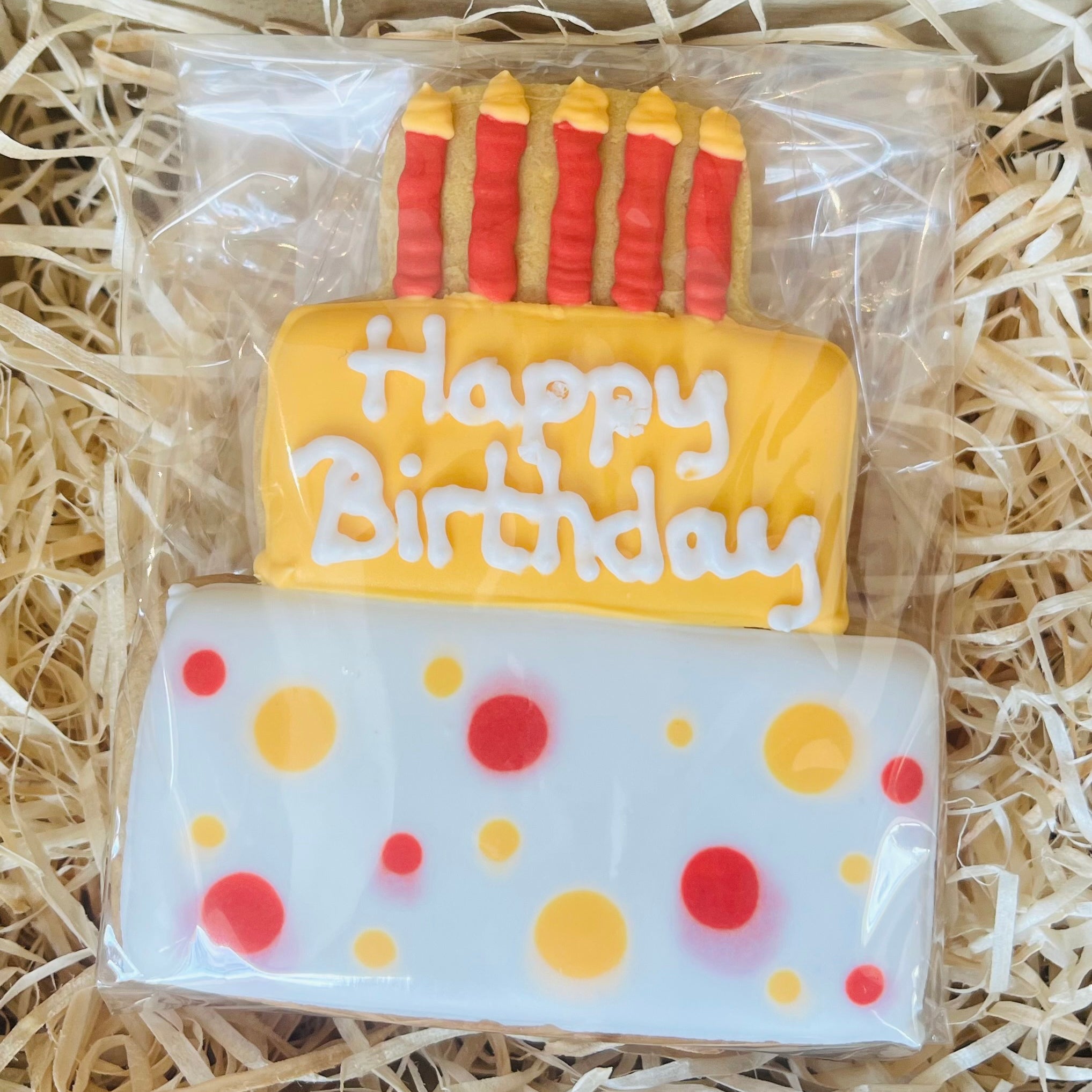 Cookie designed like a birthday cake with 'Happy Birthday' text and candles on a bed of straw.