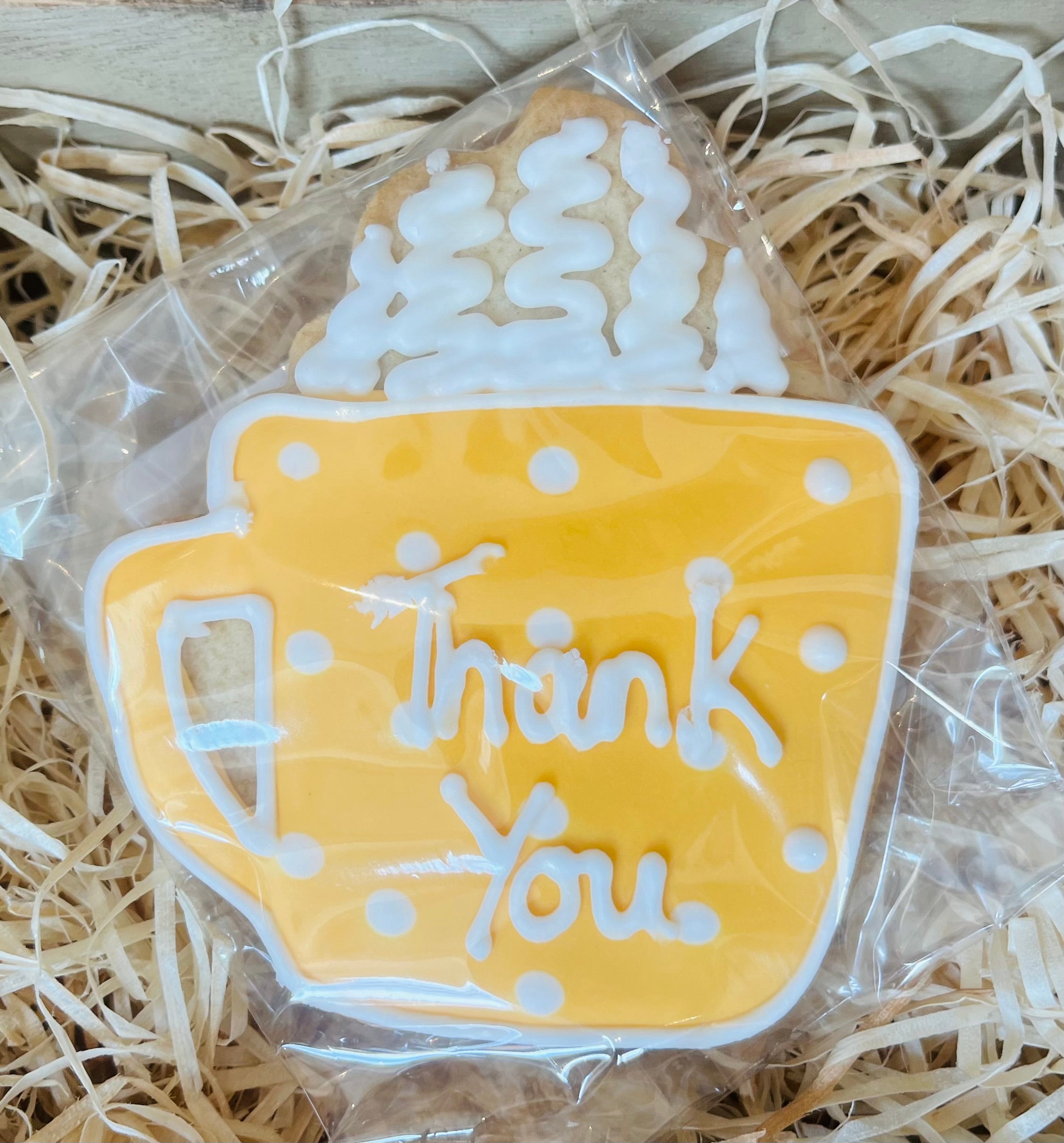 Decorative cookie shaped like a mug with 'Thank You' text, wrapped in clear plastic on straw.