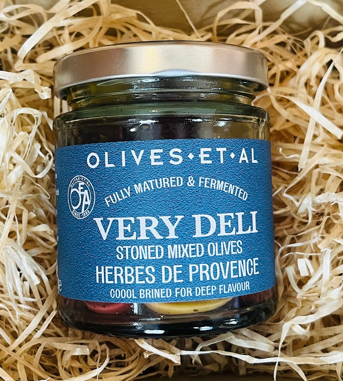 Jar of olives with a blue label on a bed of straw