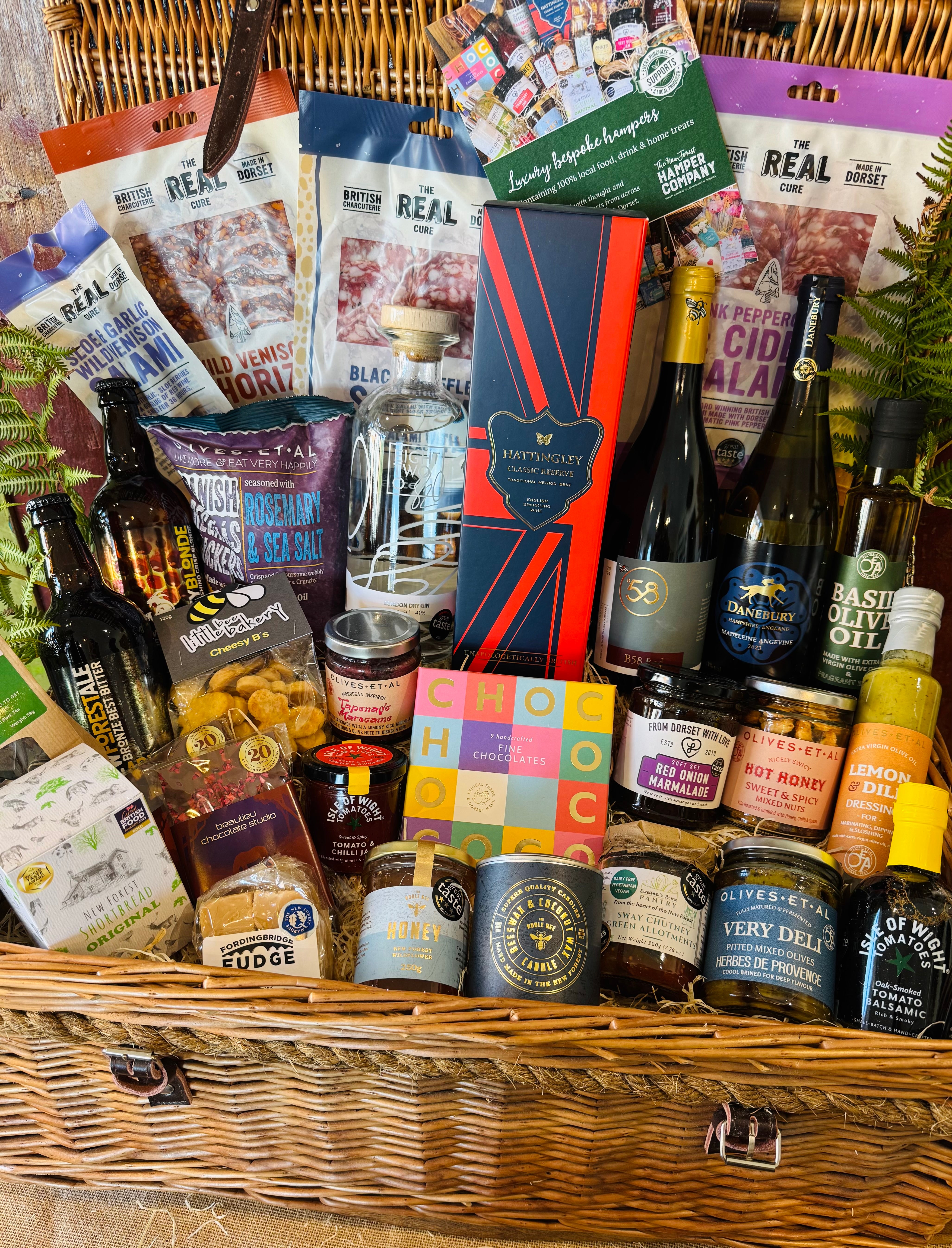 Close view of The Ultimate Hampshire & Dorset Hamper showing Chococo handcrafted chocolates, red onion marmalade, hot honey nuts, Sway Chutney, Herbes de Provence olives, New Forest wildflower honey and a Noble Bee beeswax candle