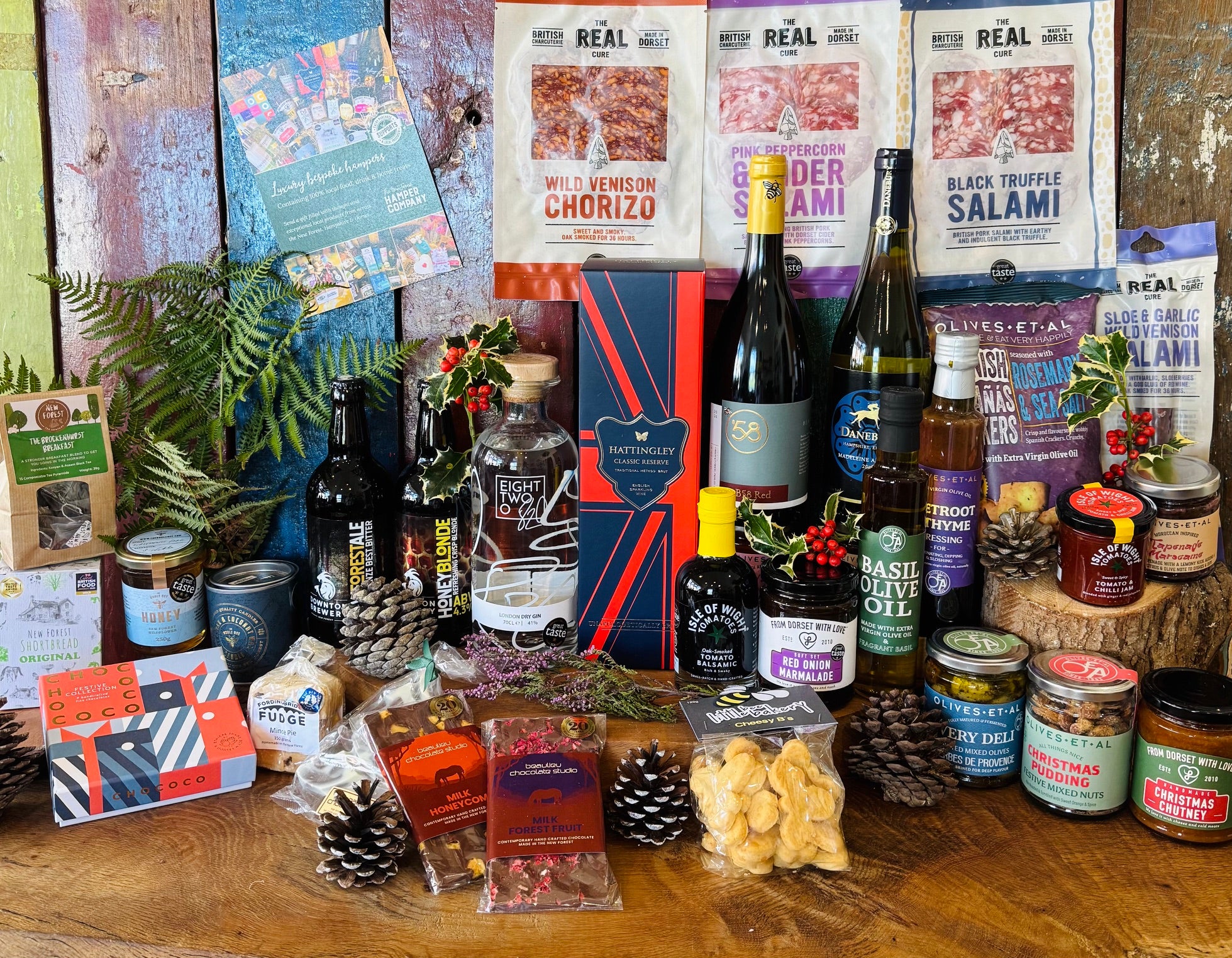 The Ultimate Hampshire & Dorset Christmas Hamper in display format - Hattingley Valley Classic Reserve, B58 red, Danebury Madeleine Angevine, 820 Spirits London Dry Gin and two Downton Brewery ales with four Real Cure salamis, Chococo festive chocolates, Olives et Al preserves and the 24 inch willow basket
