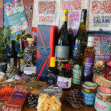 Full festive contents laid out - Christmas chutney, Christmas pudding festive mixed nuts, red onion marmalade, oak-smoked tomato balsamic, tomato and chilli jam, basil olive oil, beetroot and thyme dressing, Herbes de Provence olives and New Forest wildflower honey