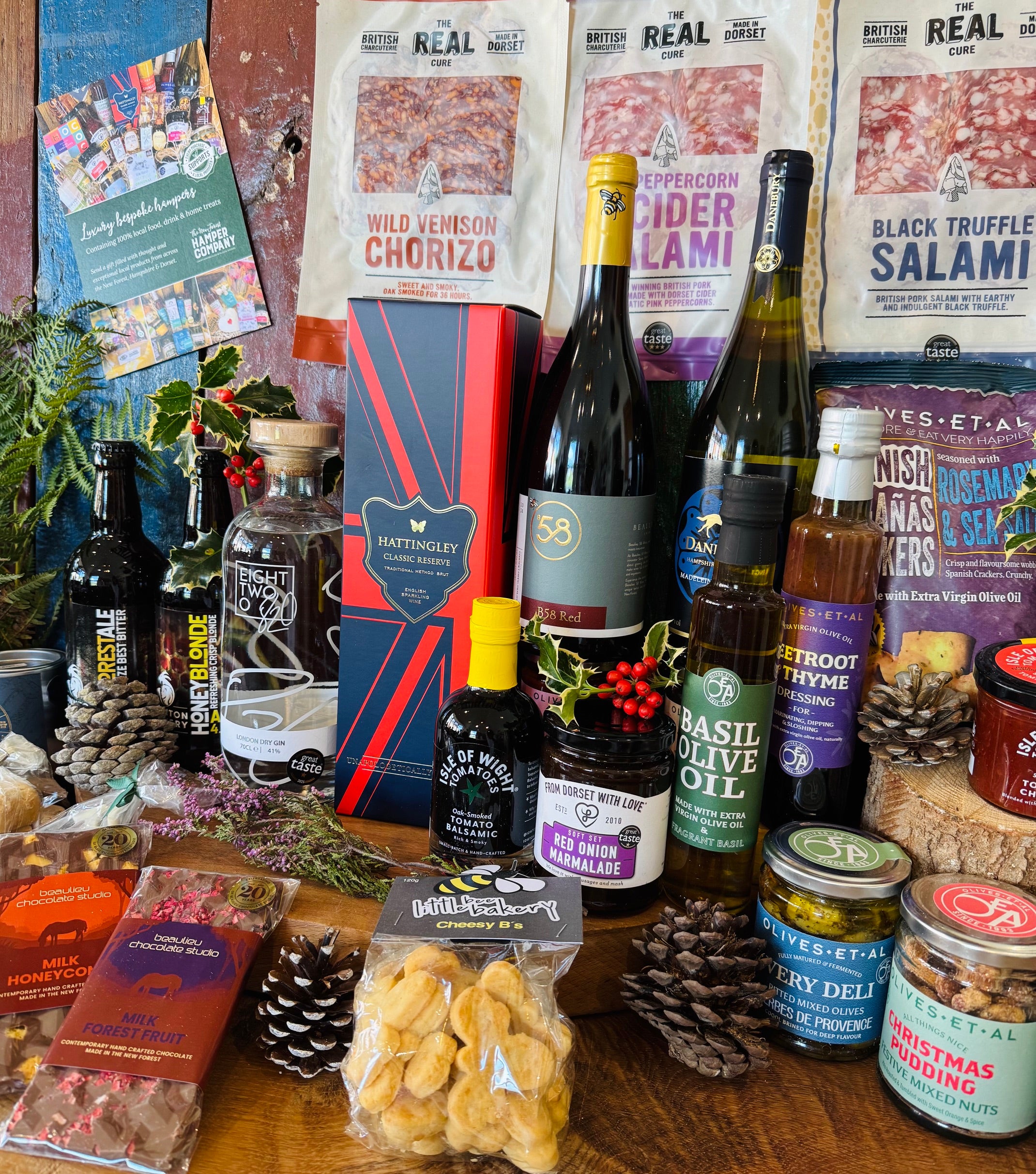 Full festive contents laid out - Christmas chutney, Christmas pudding festive mixed nuts, red onion marmalade, oak-smoked tomato balsamic, tomato and chilli jam, basil olive oil, beetroot and thyme dressing, Herbes de Provence olives and New Forest wildflower honey
