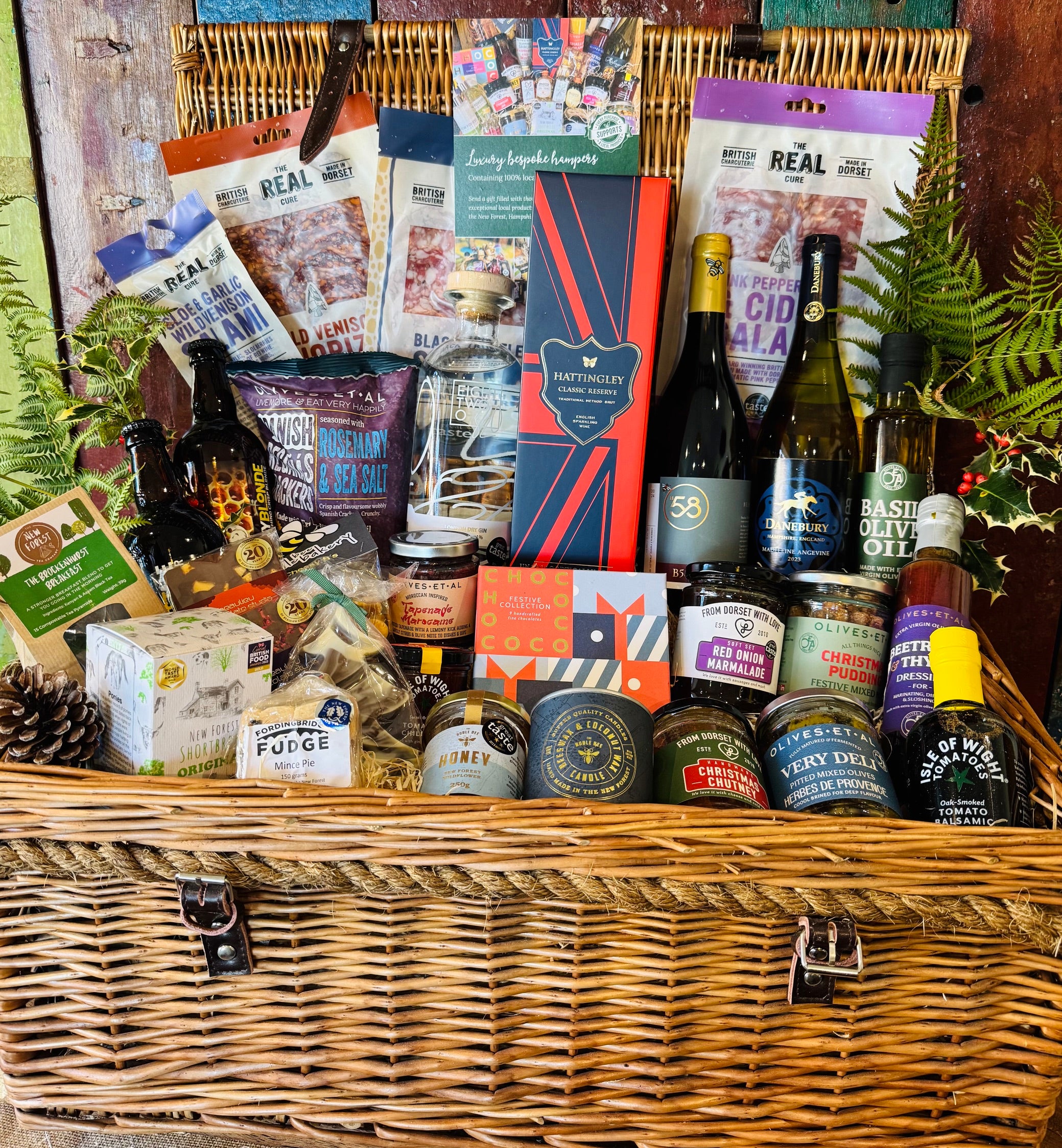 The Ultimate Hampshire & Dorset Christmas Hamper - a 24 inch lidded willow basket with Hattingley Valley sparkling wine, B58 and Danebury wines, 820 Spirits gin, Downton ales, Real Cure charcuterie, Chococo festive chocolates and Christmas preserves, dressed with fern and holly