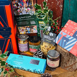 The Hattingley Festive Indulgence Hamper laid out - Hattingley Classic Reserve English sparkling wine, Real Cure Christmas snacking salami, Chococo Festive Collection, Olives et Al Pigs in Blankets nuts and Moroccan tapenade, From Dorset With Love Christmas chutney, Little Bee cheesy stars and Summerdown peppermint crisps