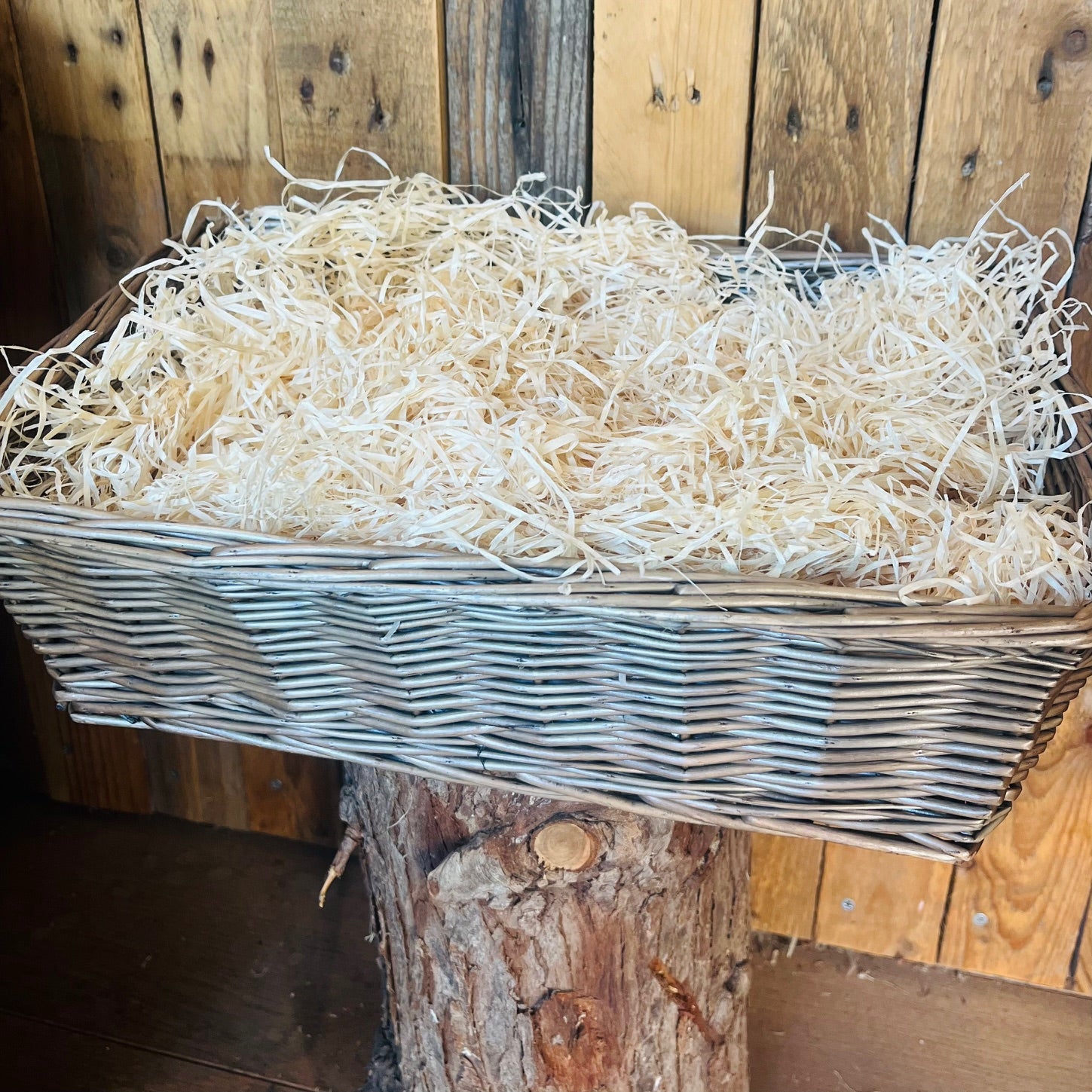 Wicker basket filled with straw against a wooden background