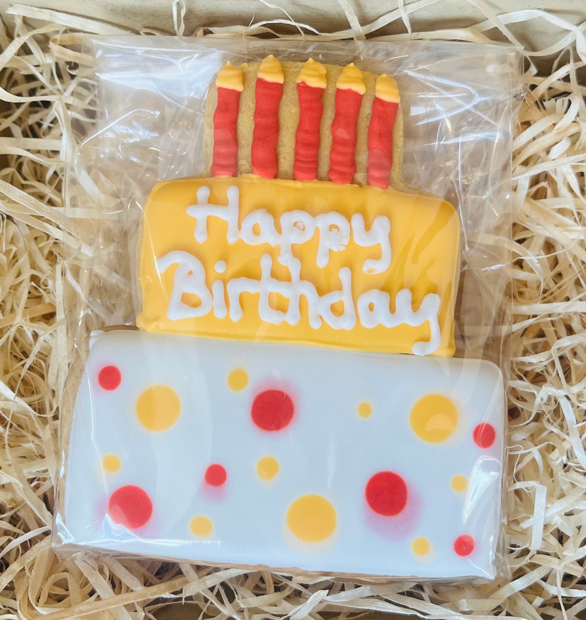 Cookie designed like a birthday cake with 'Happy Birthday' text and candles on a bed of straw.