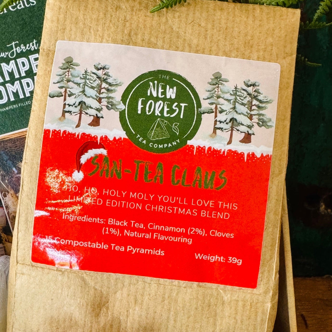 A kraft paper tea bag package labeled 'New Forest Tea Company' and 'San-Tla Claus', shown in a gift box with pinecones and evergreen branches around it.