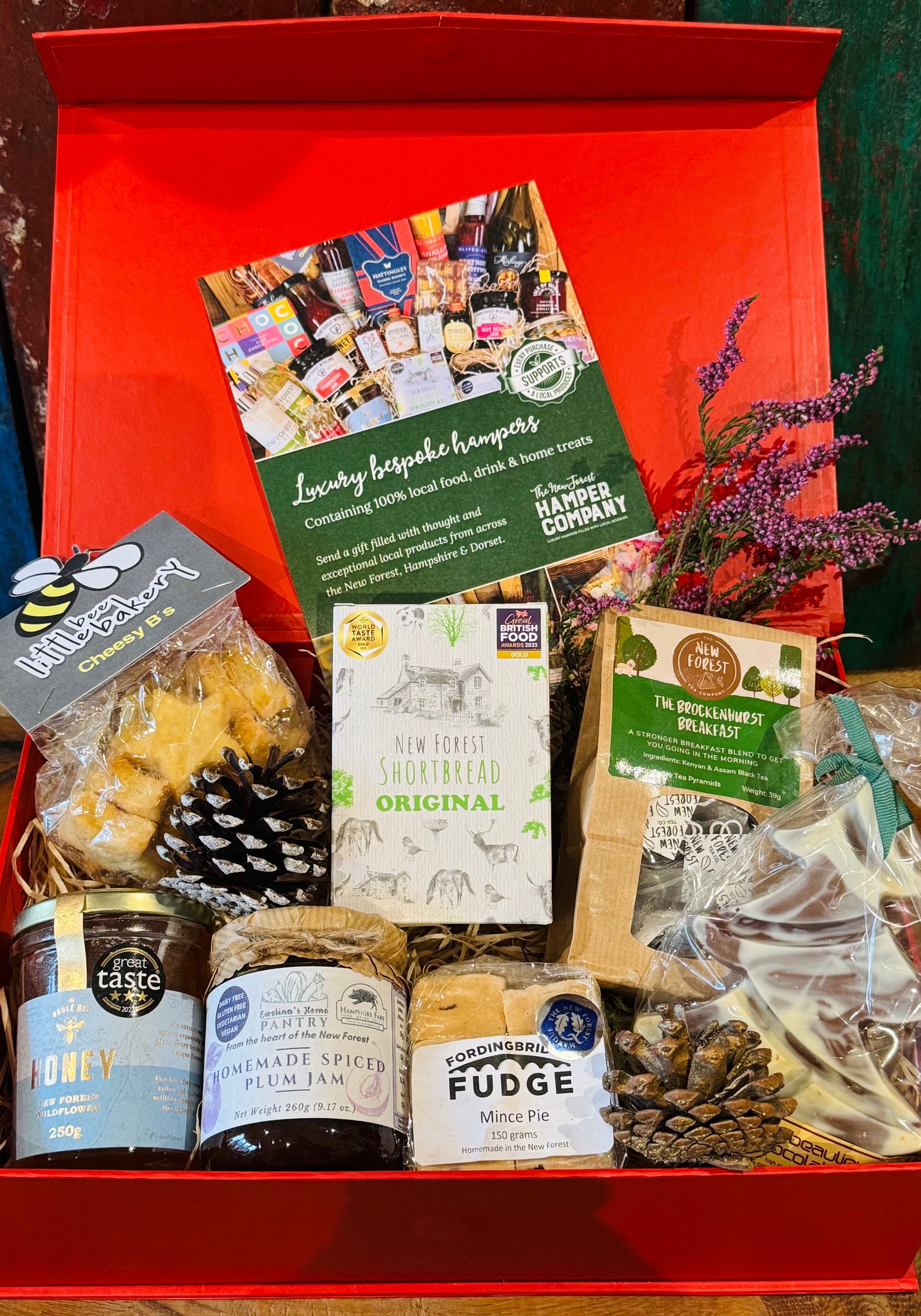 New Forest Festive Favourites Giftbox, a red gift box packed with shortbread, wildflower honey, cheesy stars, mince pie fudge, spiced plum jam, Brockenhurst Breakfast tea and a Beaulieu chocolate Christmas tree
