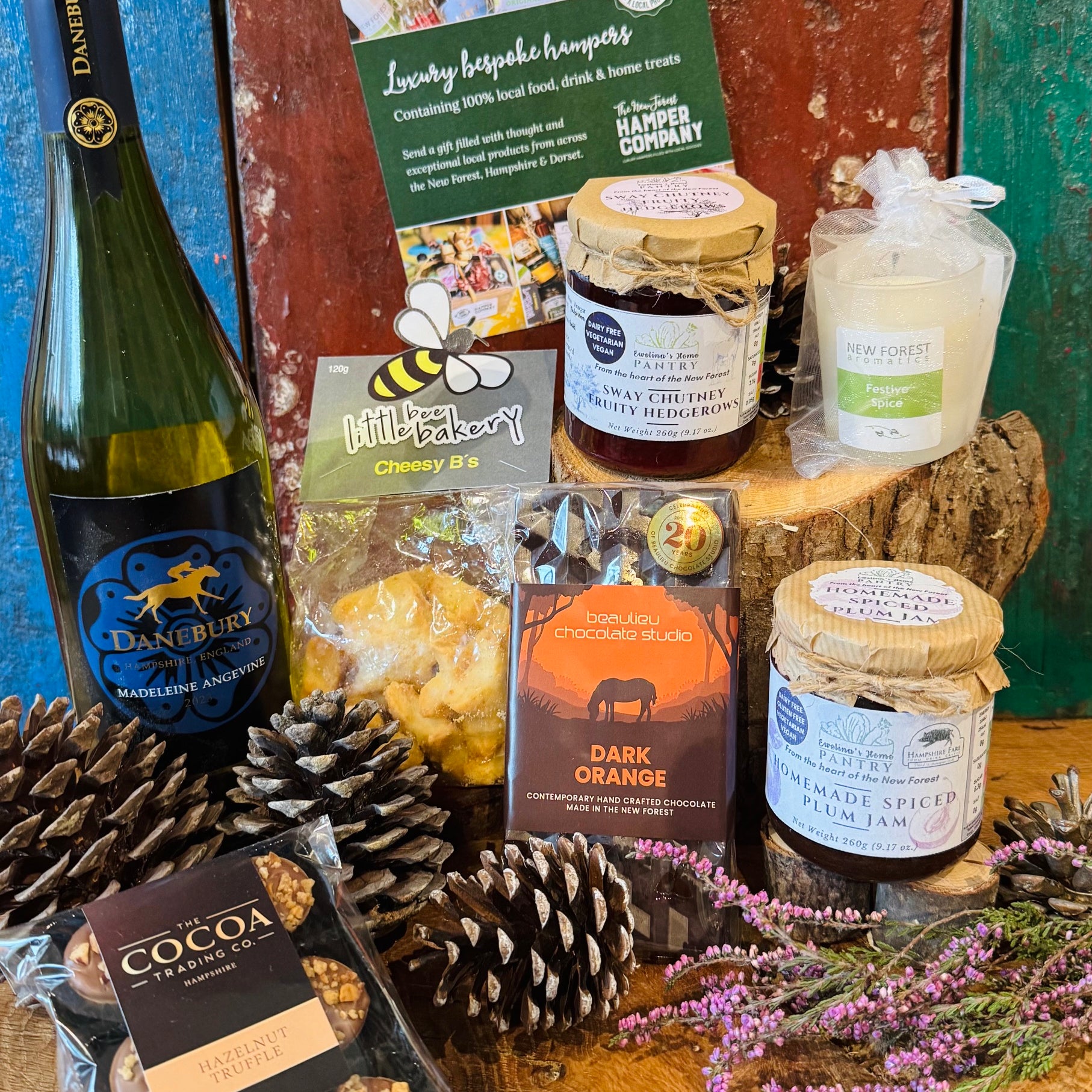 The Festive Danebury Wine Hamper contents displayed side by side, showing the Hampshire white wine, cheesy stars, chutney, spiced plum jam, chocolates and festive spice candle
