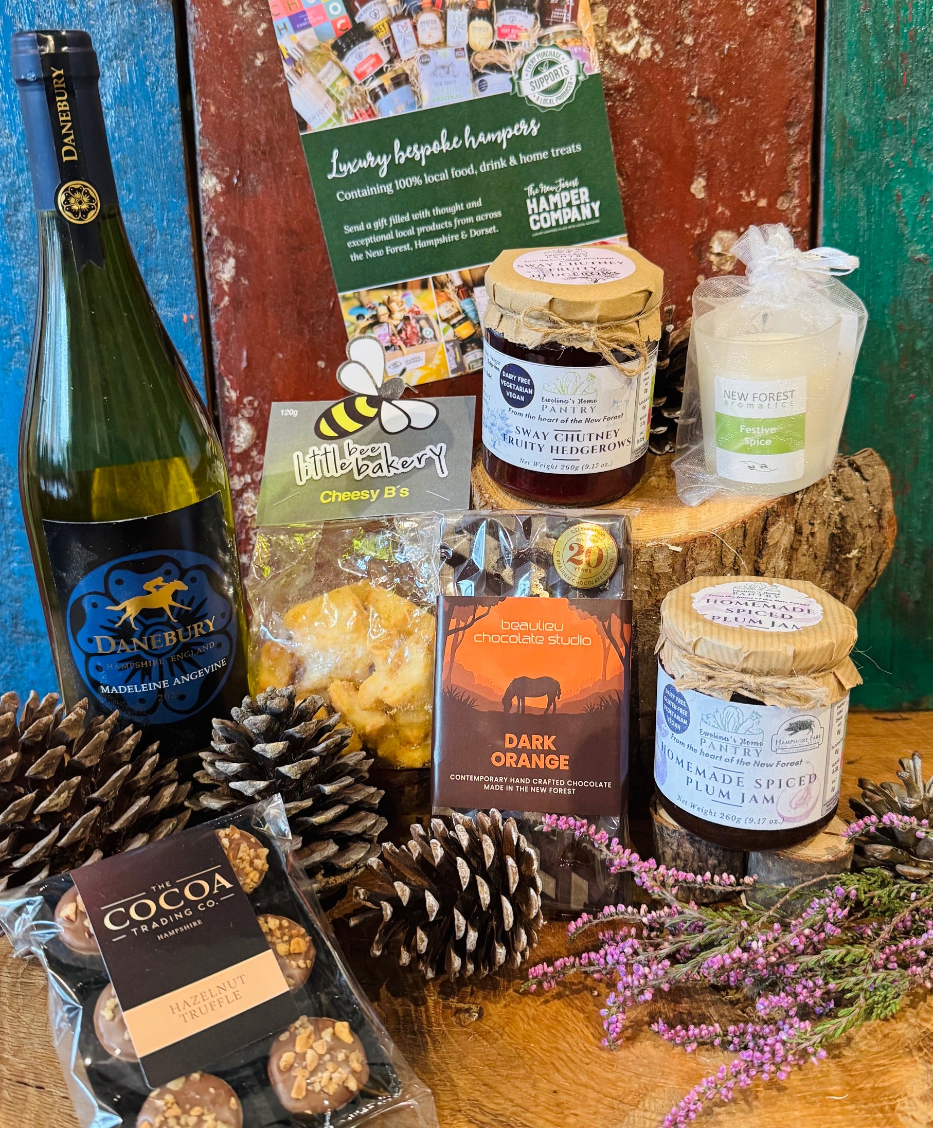 The Festive Danebury Wine Hamper contents displayed side by side, showing the Hampshire white wine, cheesy stars, chutney, spiced plum jam, chocolates and festive spice candle
