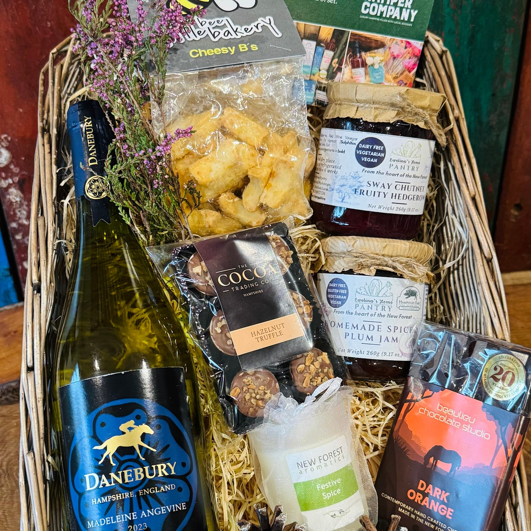 The Festive Danebury Wine Hamper in a large antique willow basket, with Danebury Madeleine Angevine white wine, Cheesy Stars, Sway chutney, spiced plum jam, a Festive Spice candle and New Forest chocolates