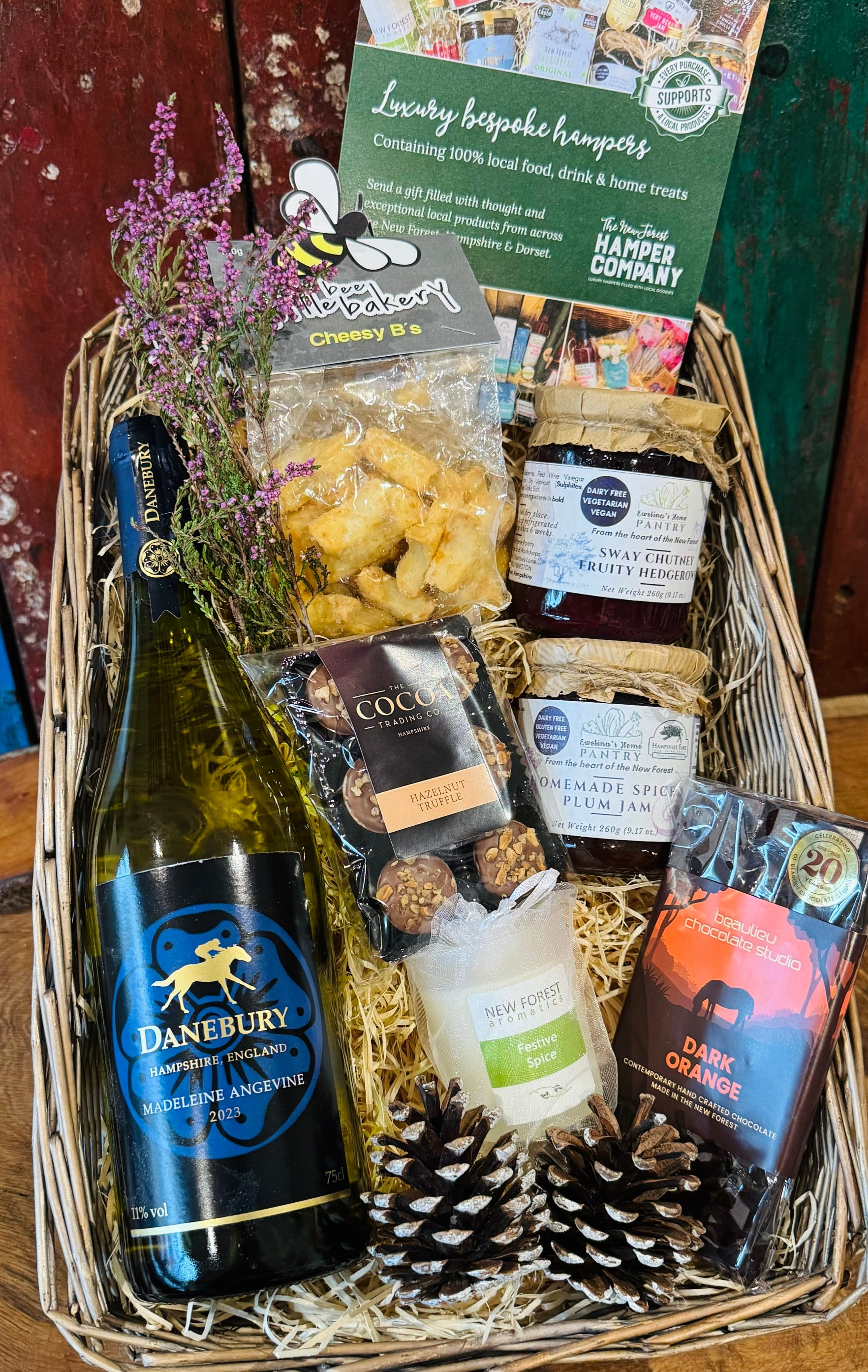 The Festive Danebury Wine Hamper in a large antique willow basket, with Danebury Madeleine Angevine white wine, Cheesy Stars, Sway chutney, spiced plum jam, a Festive Spice candle and New Forest chocolates