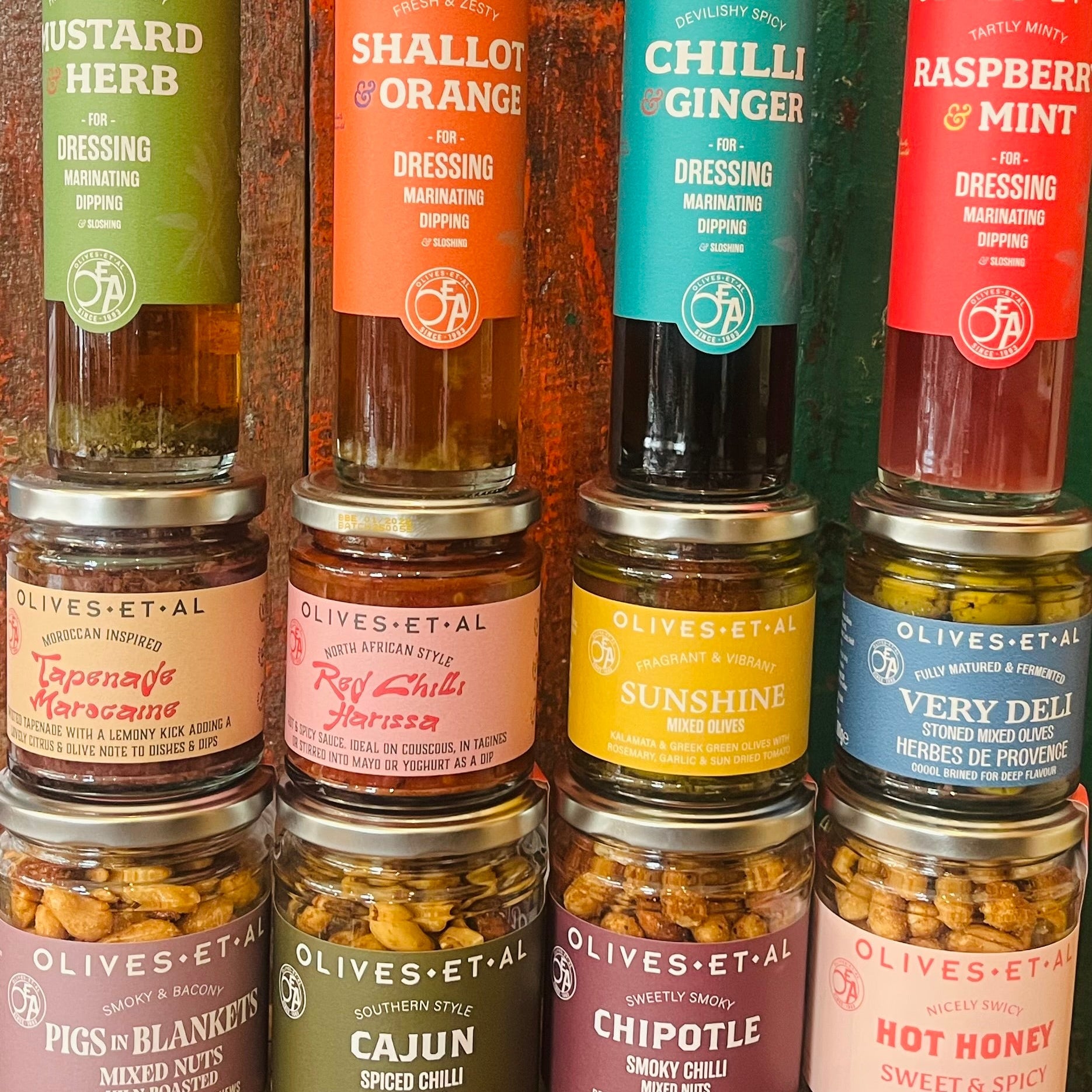 Collection of Olives Et Al food products including dressings and nuts on a wooden surface.