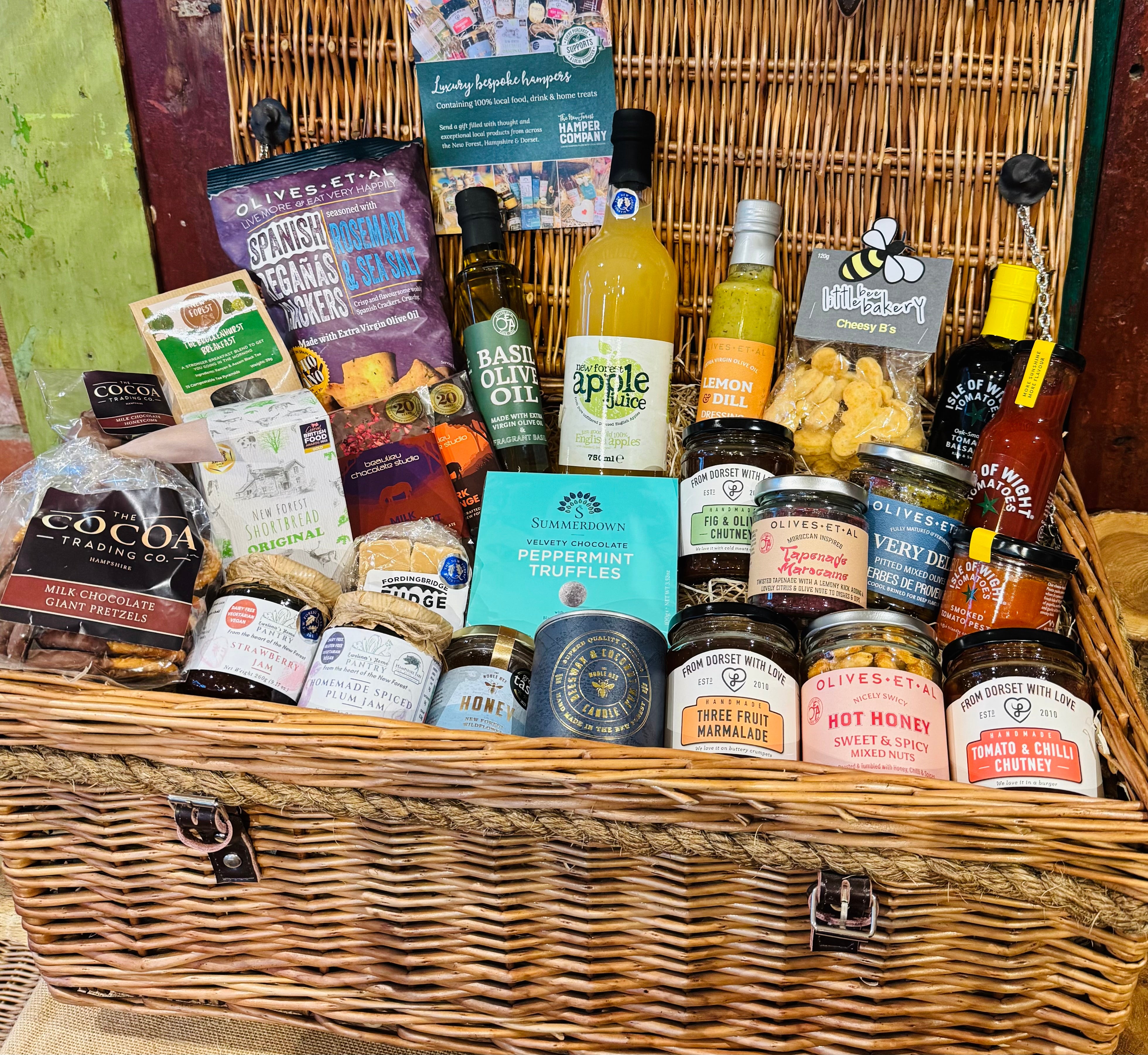 The Ultimate Hampshire & Dorset Goodies Hamper - our largest alcohol-free hamper, a 24 inch lidded willow basket with twenty-seven items: Cheesy B's, Spanish Reganas crackers, Herbes de Provence olives, Moroccan tapenade, hot honey nuts, Olives et Al oils and dressings, Isle of Wight preserves, chocolates, shortbread, apple juice and a Noble Bee beeswax candle