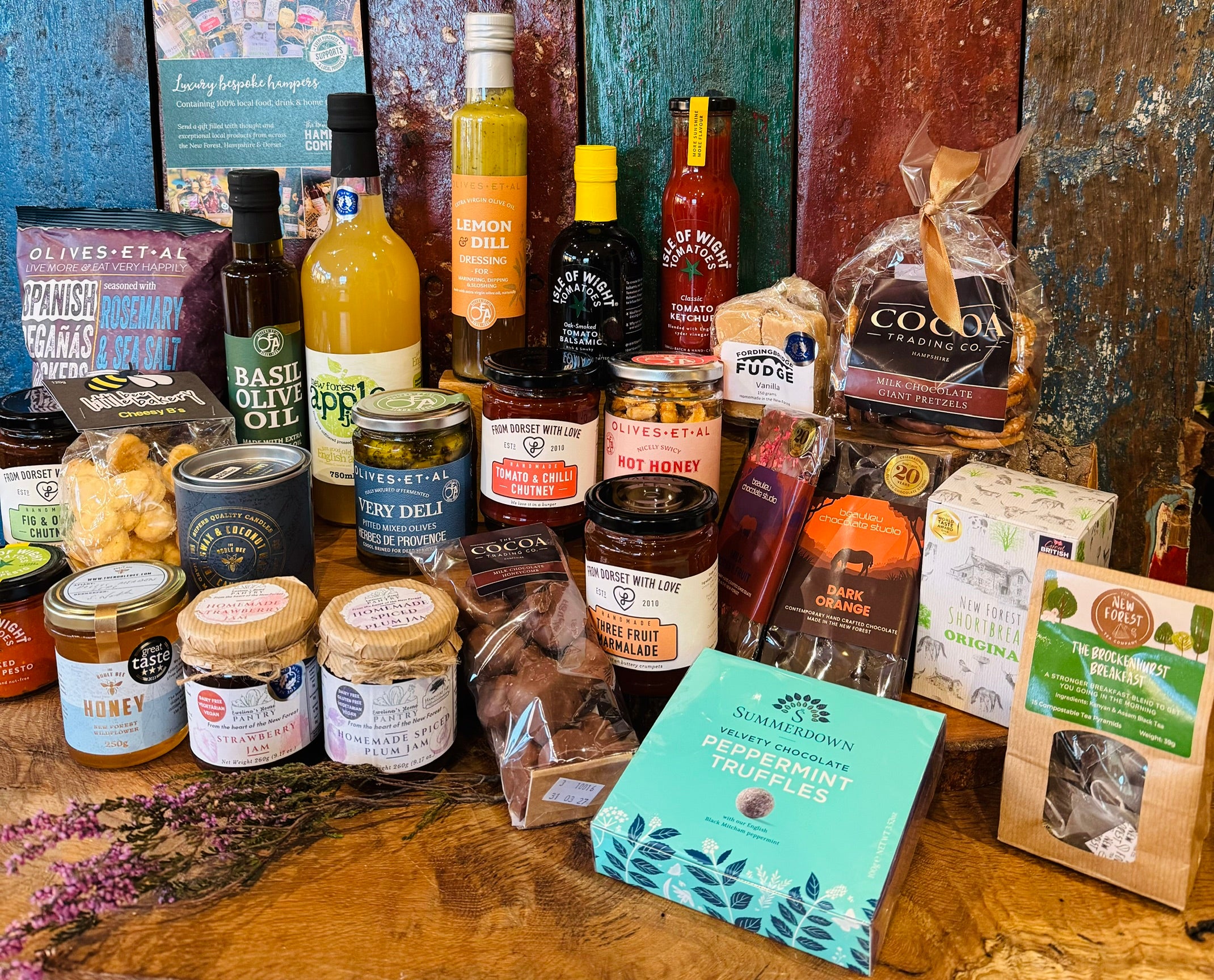 Display shot of The Ultimate Hampshire & Dorset Goodies Hamper - pressed New Forest apple juice, Brockenhurst Breakfast tea, Noble Bee wildflower honey and the Hay Honey & Amber beeswax candle alongside the local preserves and chocolates