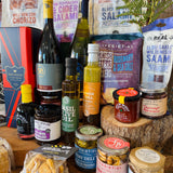 Thirty-item display of The Ultimate Hampshire & Dorset Hamper - Hampshire sparkling wine, red and white wine, New Forest gin, two local ales, charcuterie, cheese biscuits and crackers, olives and tapenade, oils and dressings, preserves, honey, chocolates and a beeswax candle with the 24 inch willow basket