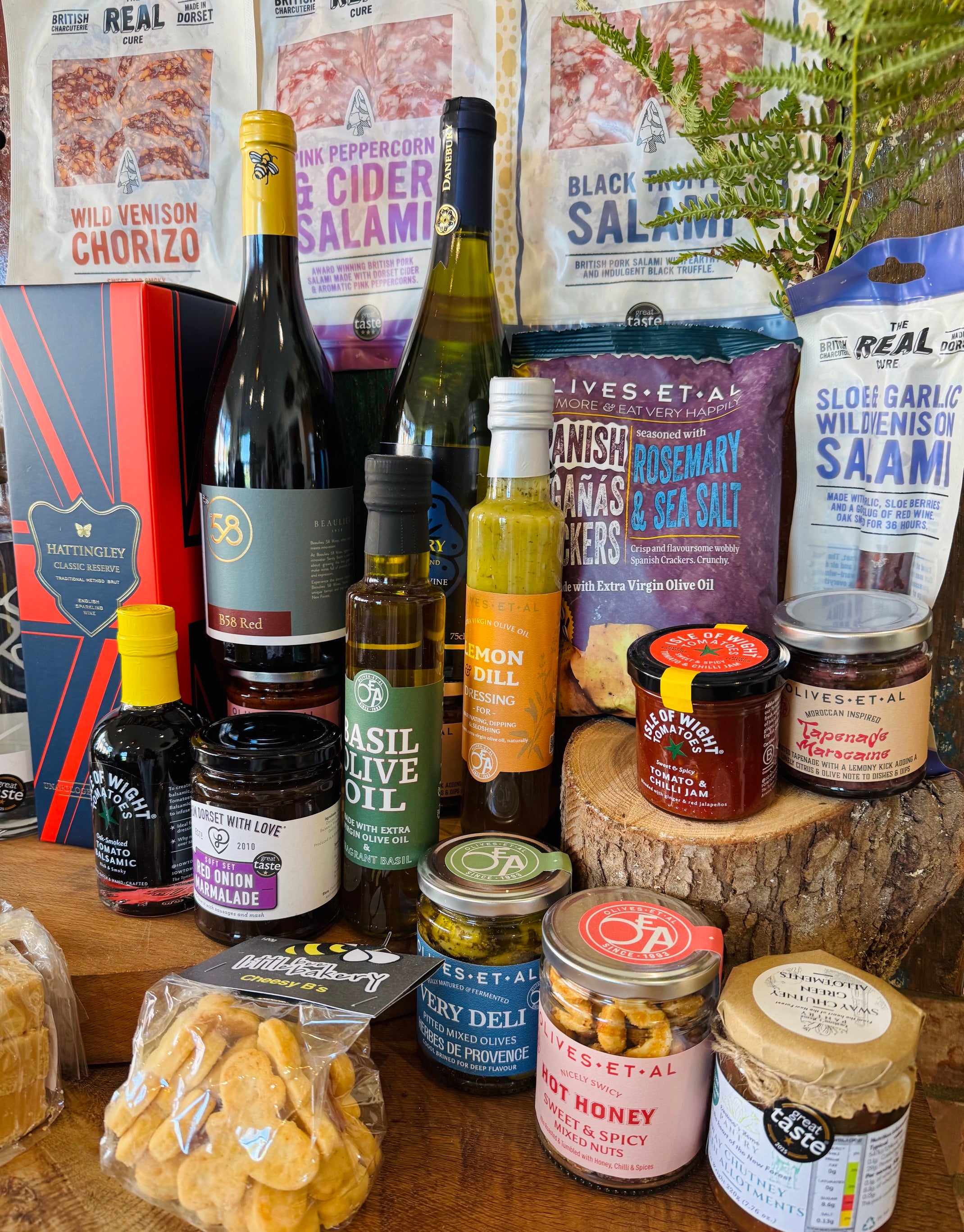 Thirty-item display of The Ultimate Hampshire & Dorset Hamper - Hampshire sparkling wine, red and white wine, New Forest gin, two local ales, charcuterie, cheese biscuits and crackers, olives and tapenade, oils and dressings, preserves, honey, chocolates and a beeswax candle with the 24 inch willow basket