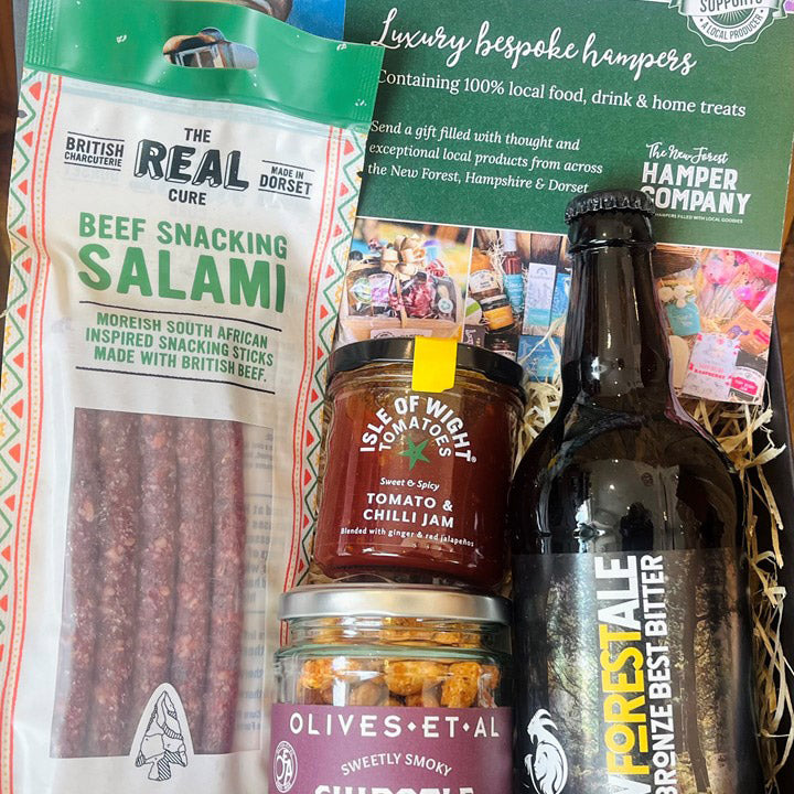 Assorted food items including salami, jam, olives, and a bottle of butter with packaging in the background.
